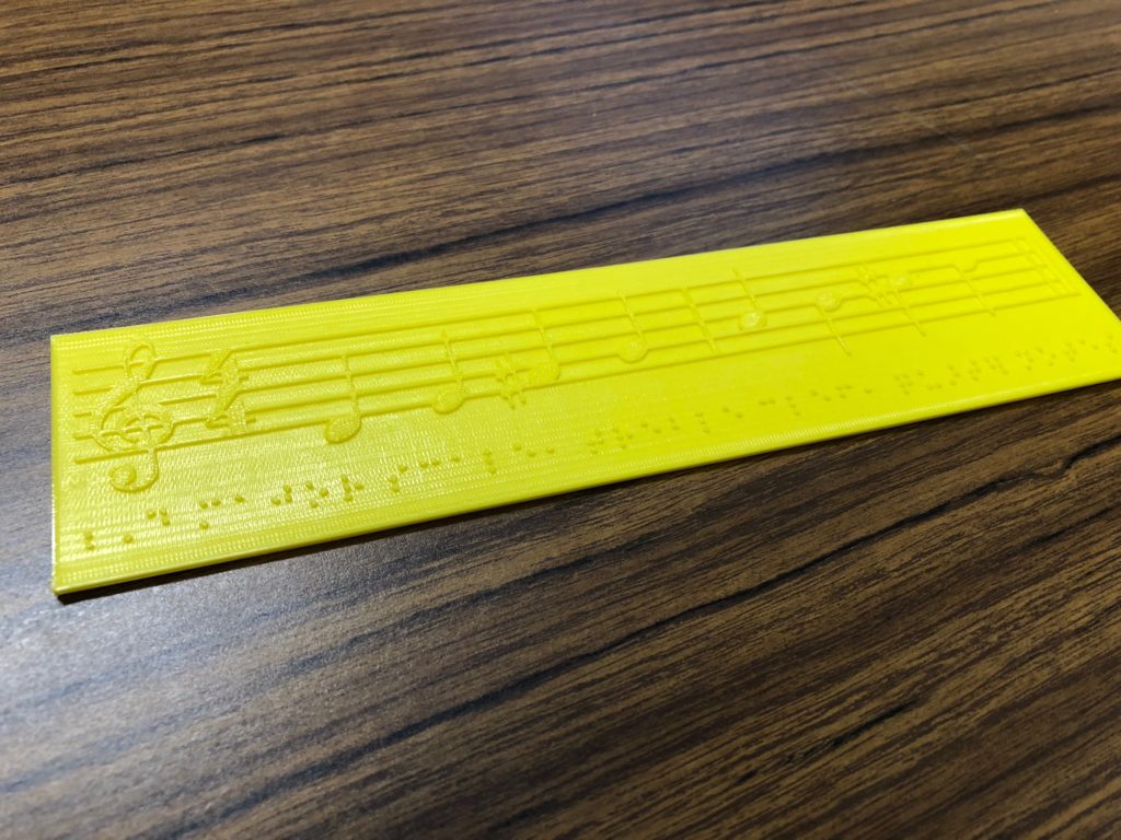 Photo of a D major scale in staff notation, embossed in plastic from a 3d printer. 